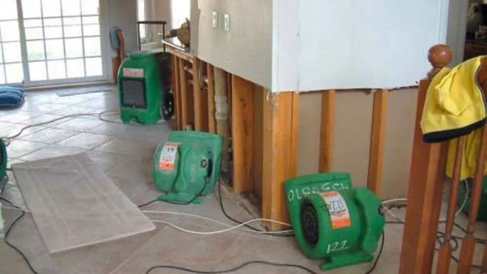 Wall opened to the studs with green air movers drying the room after water damage